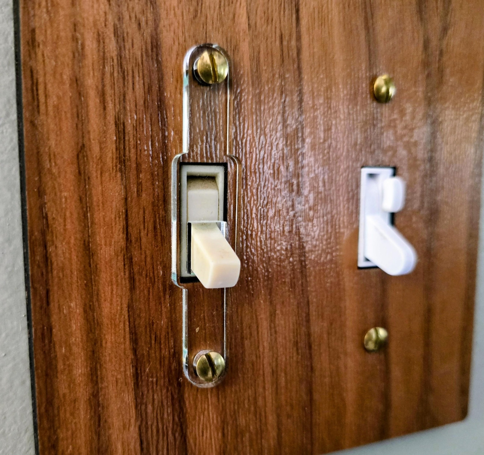 Clear acrylic toggle switch guard capping the left switch on a wood switch plate